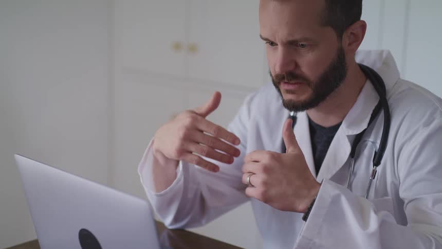 A doctor talks with someone on his laptop