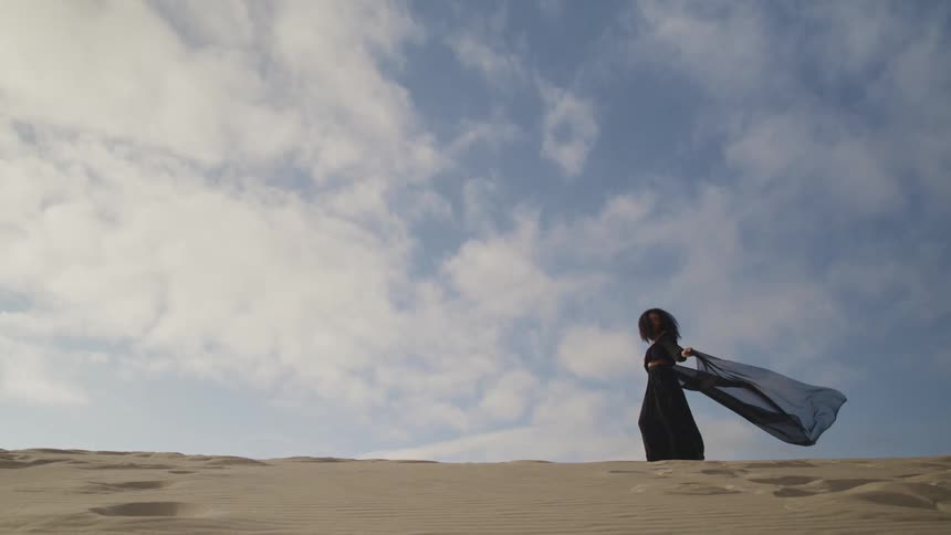 A woman holds a black scarf behind her as she poses in the desert