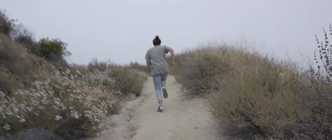 A woman runs up a dirt trail on an overcast day