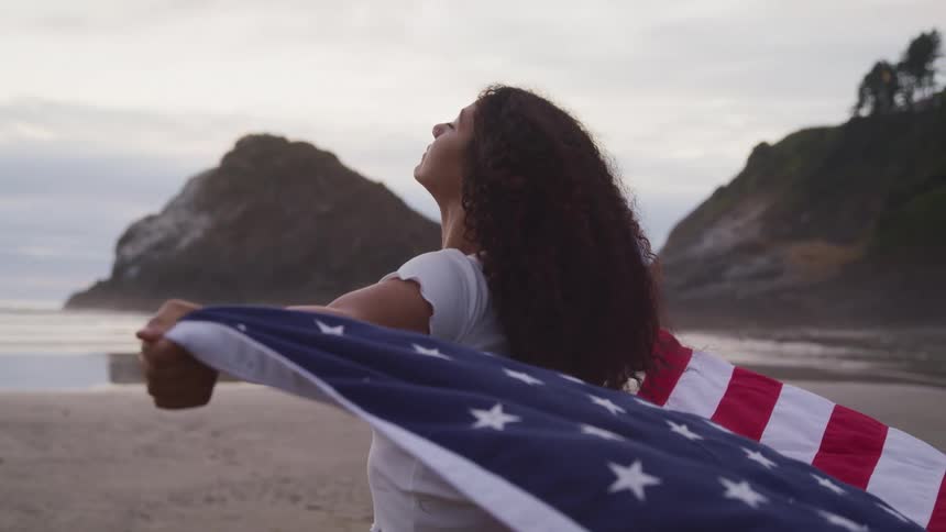 Woman holding american flag stands on beach head thrown back