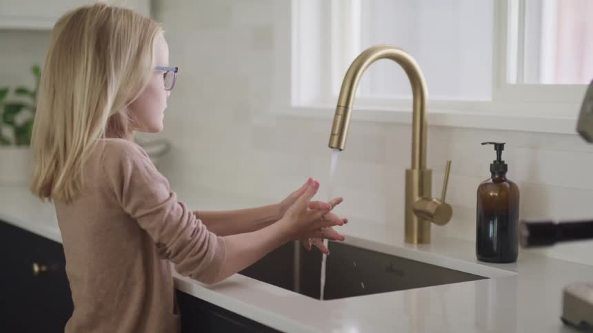 A girl with glasses washing her hands with water from a faucet