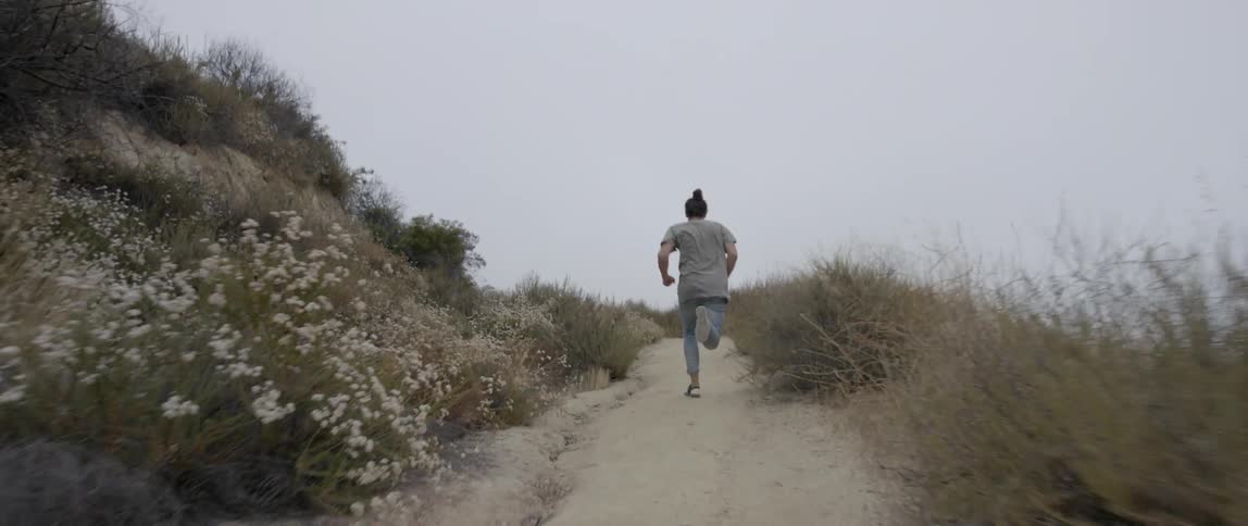A person runs up a dirt trail in an area with lots of scrub brush