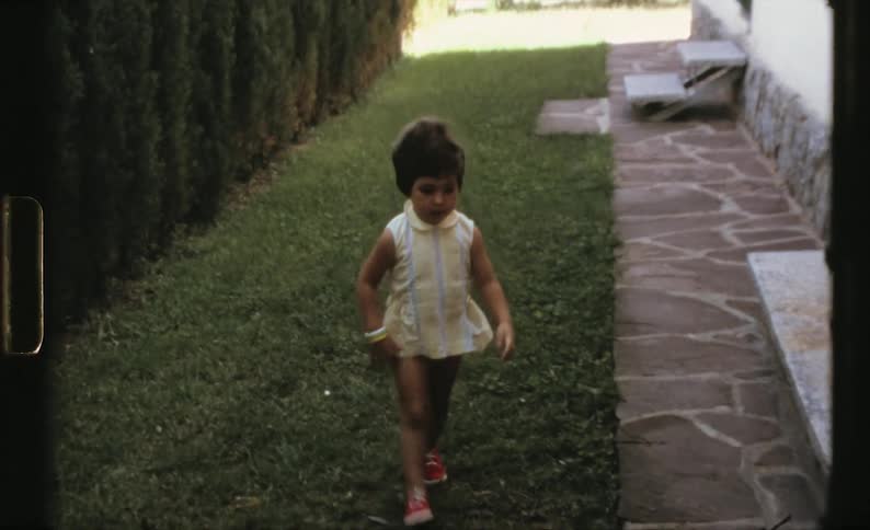 Toddler little girl with a yellow dress holding a big ball runs in the backyard