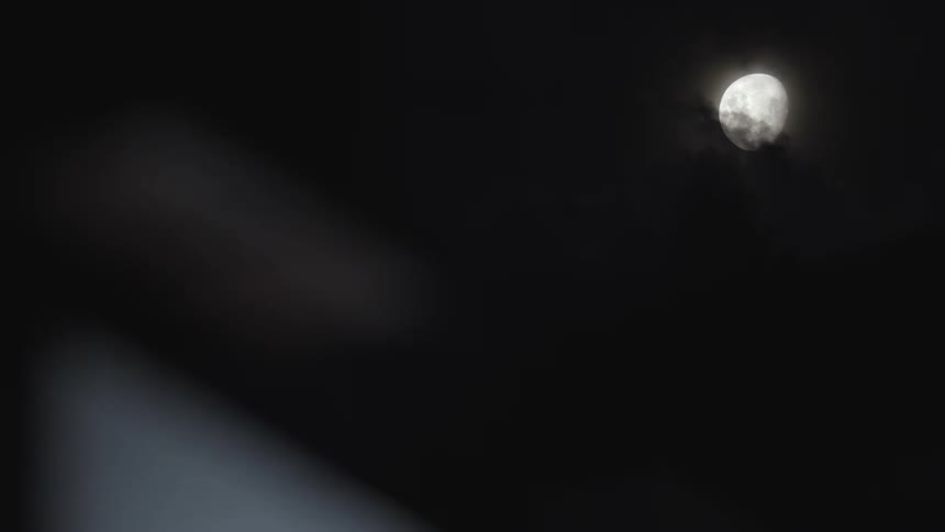Wide shot of wispy clouds moving across of the moon