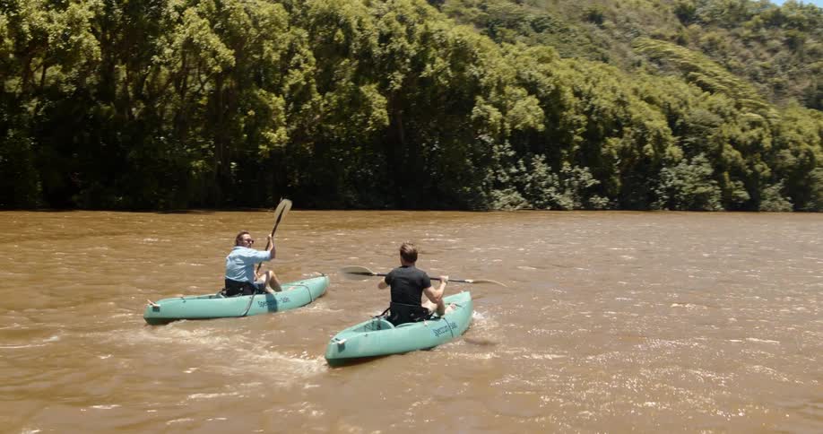 Two men each paddle a canoe in the river