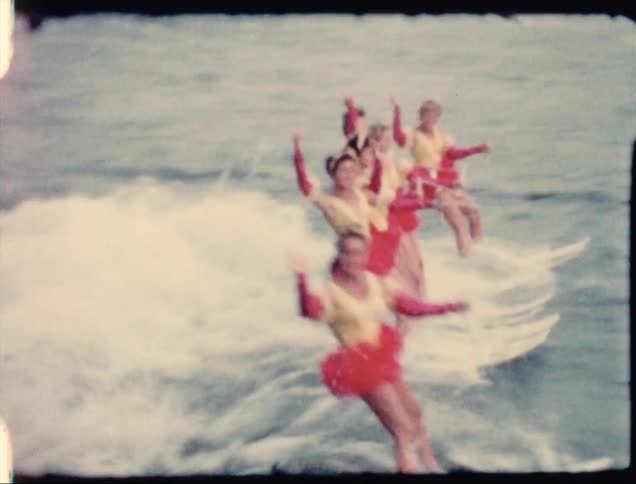 A team of female water skiers waving while riding behind a boat