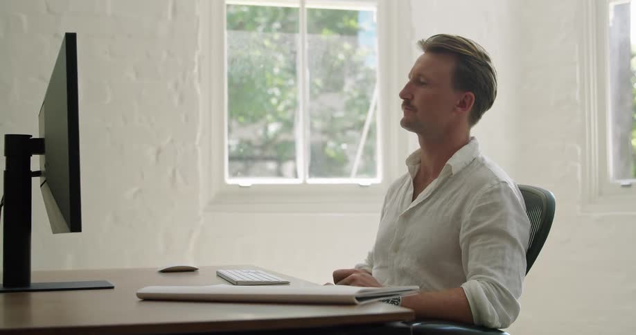 A man takes notes and types while working from home on his computer