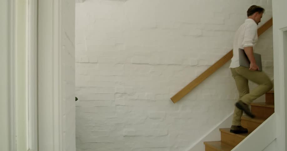 A man carries his laptop up the stairs on a bright sunny day