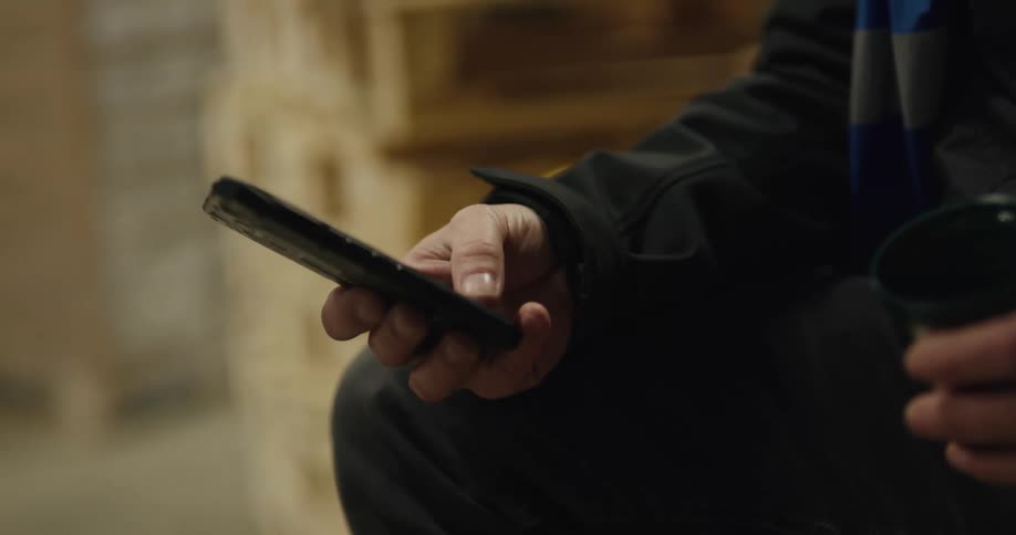 A man scrolls on his phone and takes a drink of a beverage