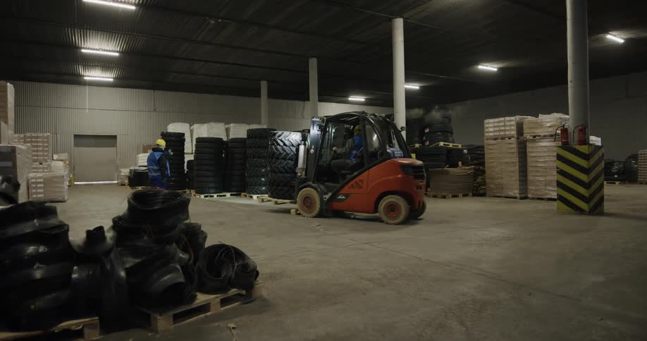 A few workers moving a pallet with a forklift in a warehouse