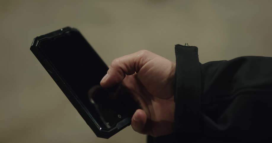 A hand holds a smart phone and scrolls and taps on a black screen with their thumb