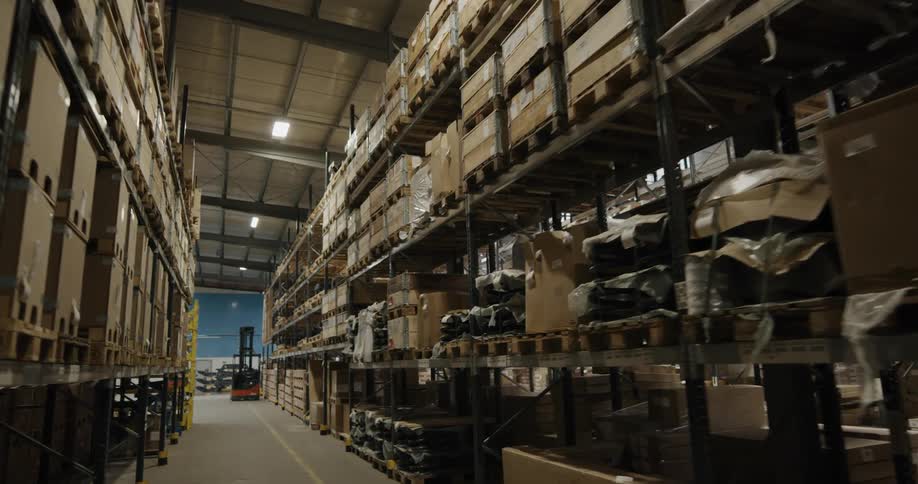 A warehouse aisle with shelves loaded with boxes and crates and a forklift at the end