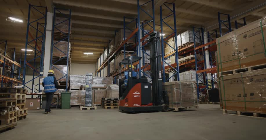 Warehouse worker uses a forklift to deliver pallets of products to a tall aisle