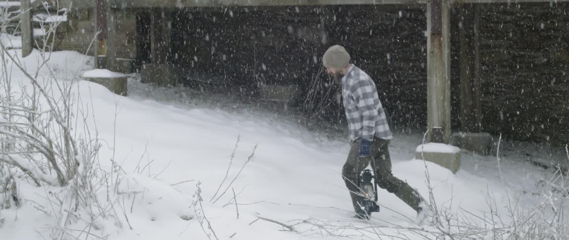 Man is walking outside carrying lantern while it snows