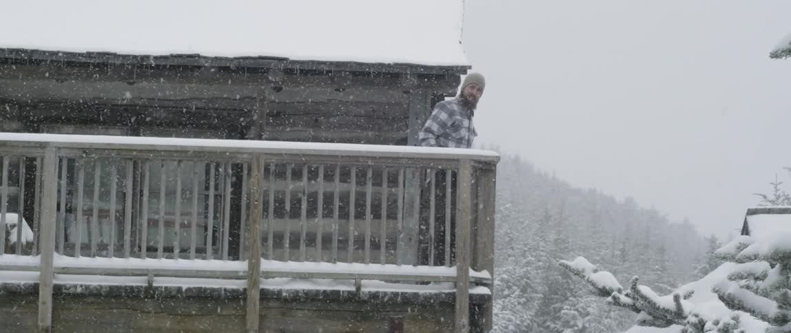 A man stands on a cabin balcony in a snowstorm