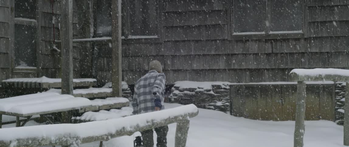 A man walks in the snow carrying a lantern