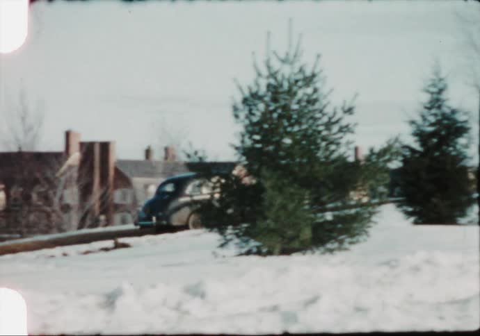 A vintage car drives along a wintery road in the 1950s