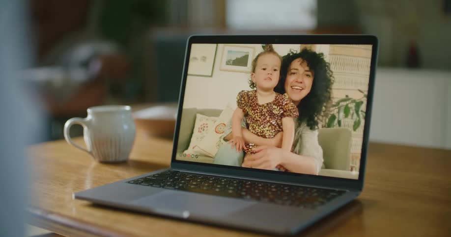 A woman on a laptop screen holds a baby and waves
