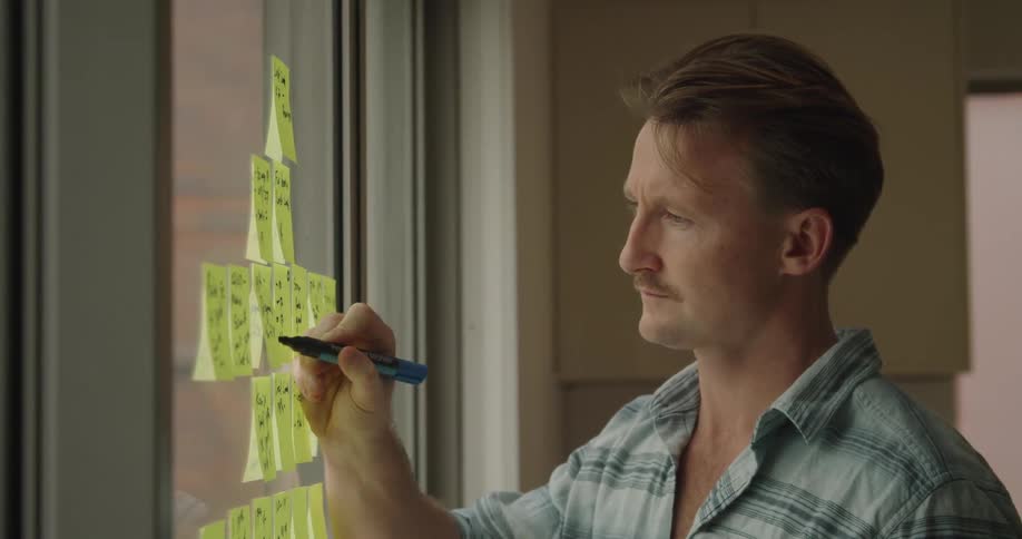 A man writes on sticky notes on a window