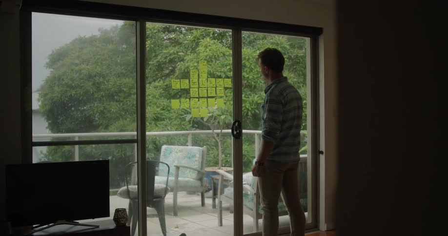 Man working in the office at home writing on post its taped in a glass door