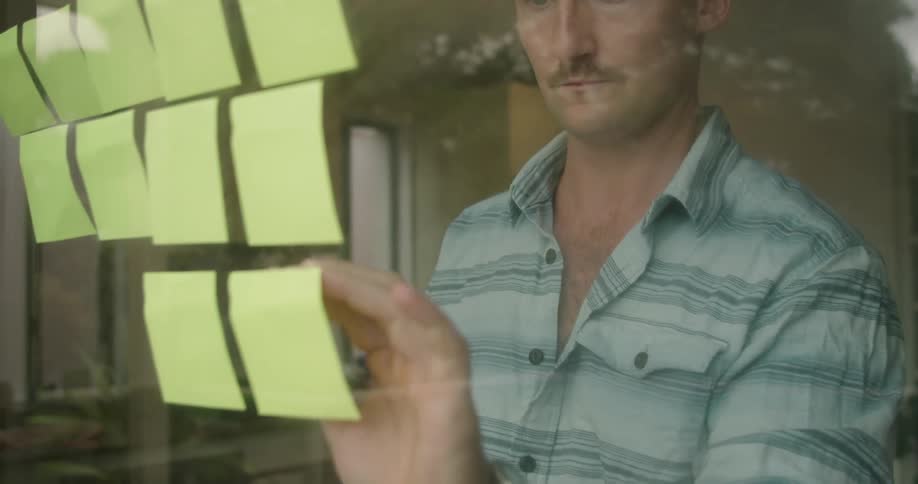 A man tapes several yellow sticky notes to his sliding glass door