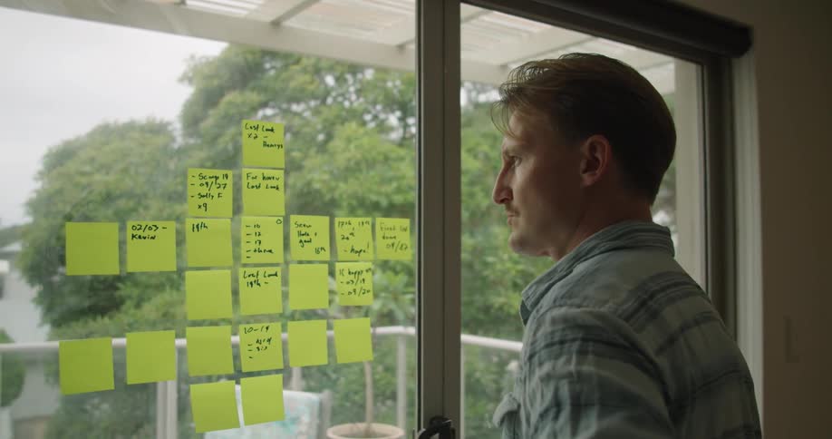Man working in the office at home writing on post its taped in a glass door