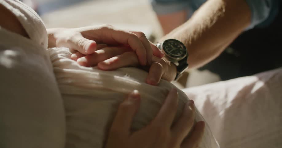 A woman caresses her husbands hand as he touches her pregnant stomach