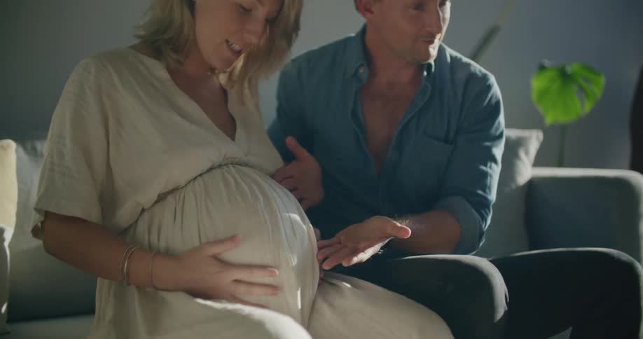 Young pregnant couple sitting in a couch in the livingroom talking on a video call