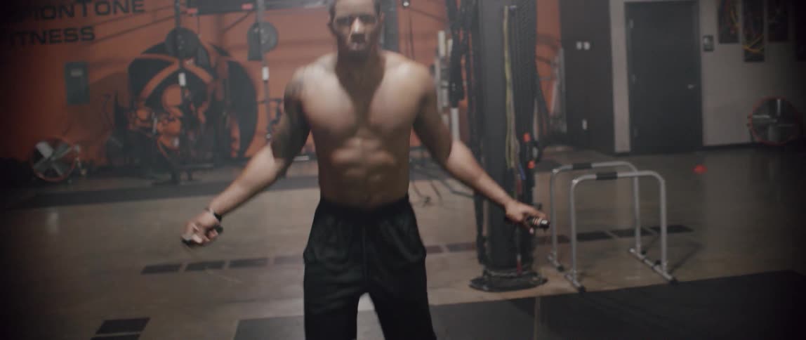 Shirtless man jumps rope in a gym