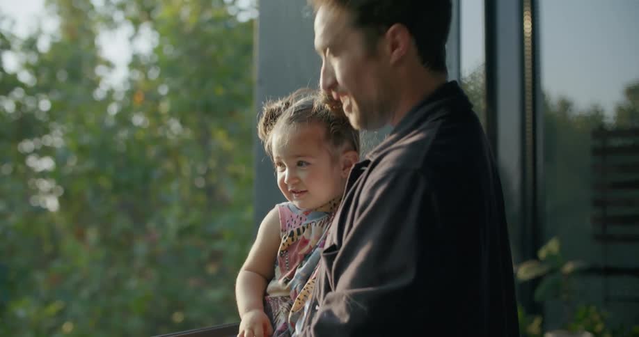 Smiling father holds daugther in his arms while playing at sunset in the living room