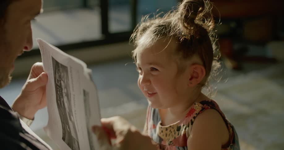 Toddler laughs as she looks at paper father holds up