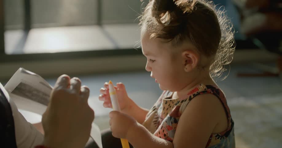 Adult hands girl a marker and holds paper up for her to draw on