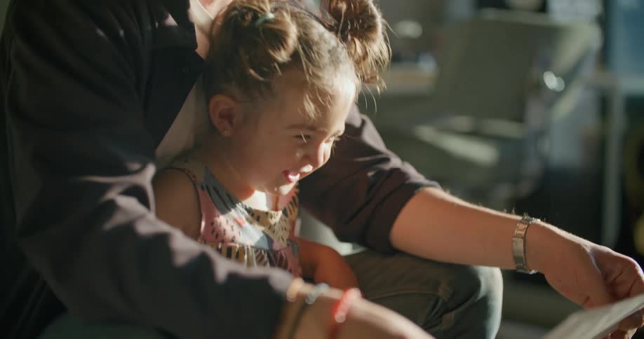 A man in a room hugging a girl and looking at a piece of paper with a wall and a chair in the background