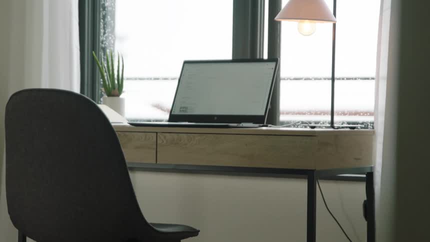 A laptop sitting on a desk in a home office in front of a window