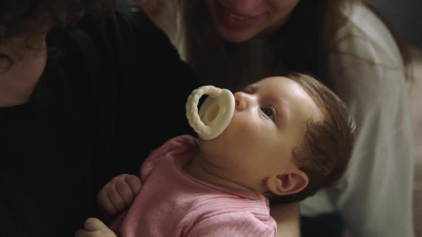 Mother and father hover around baby girl sucking on pacifier