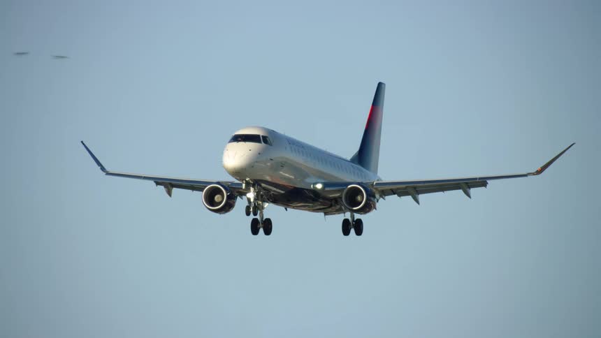 An Embraer E175 commercial passenger jet with winglets approaching landing at an airport in the evening sunset light