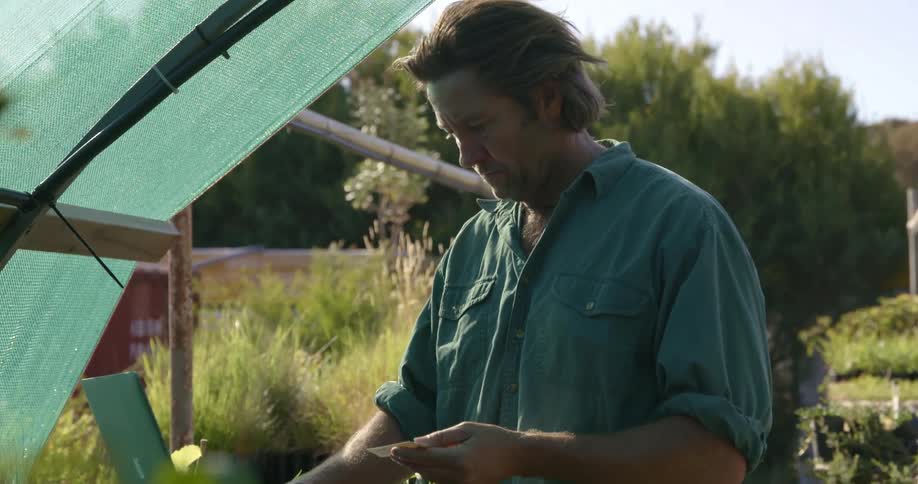 Man stands in a garden typing on a laptop