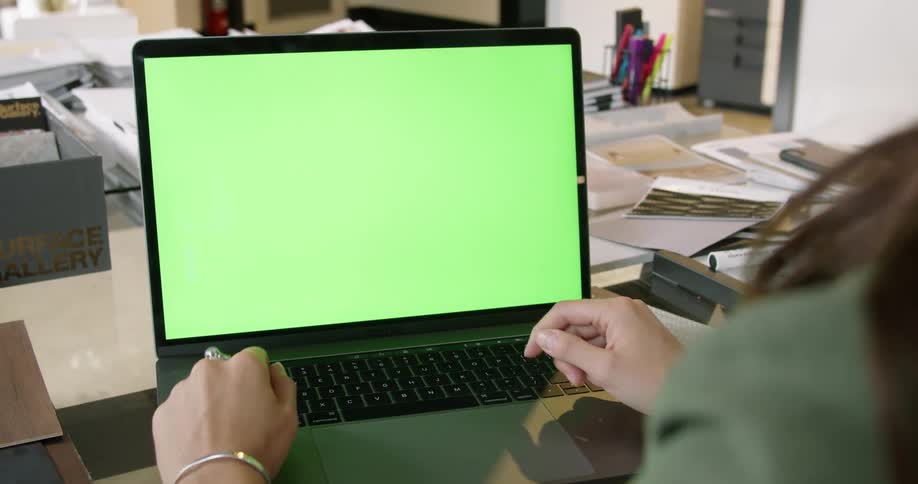 Woman sitting at a desk in front of a laptop with a replaceable green screen
