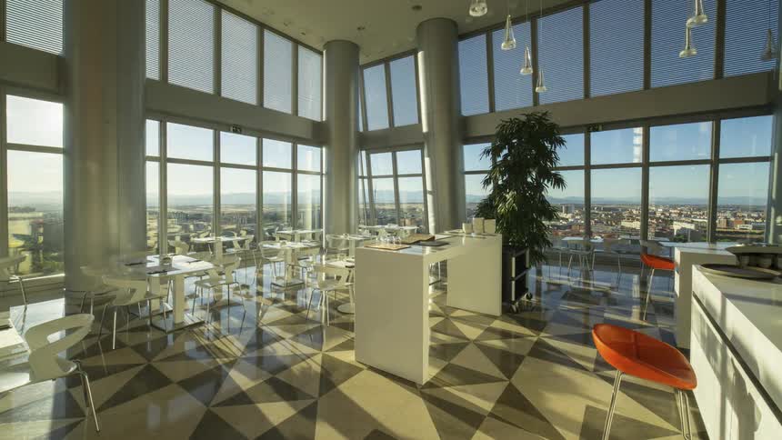 Shadows flow across floor in restaurant enclosed by floor to ceiling windows with view of city