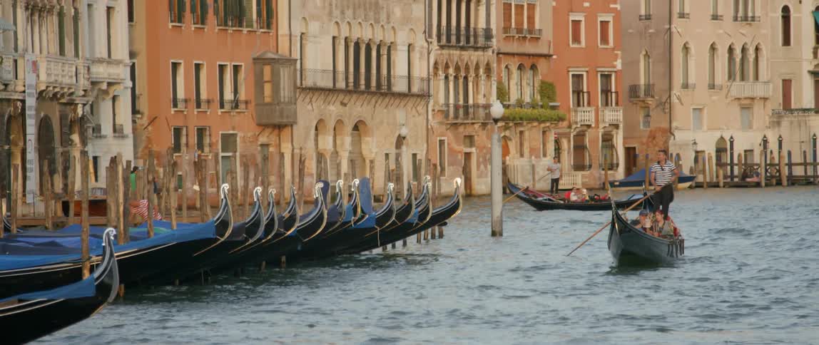 A row of boats are docked as a man rows past