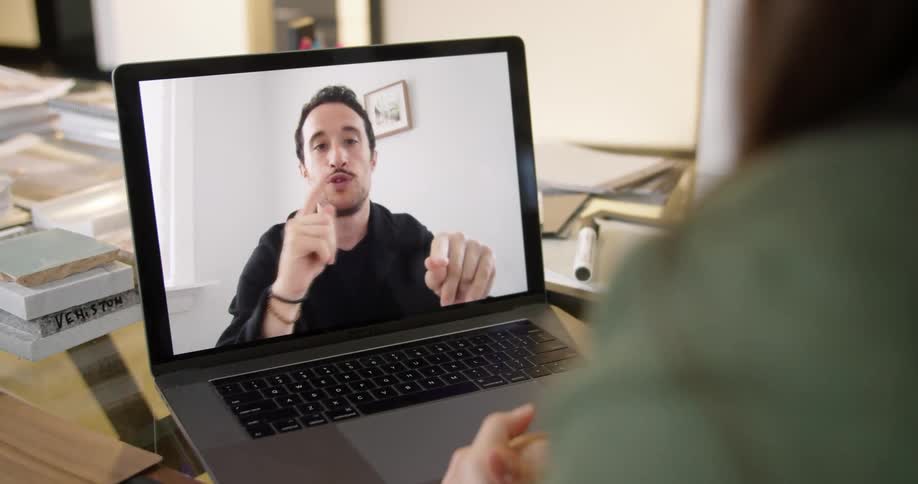 A woman uses a laptop to participate in a video chat while sitting at a table covered in products