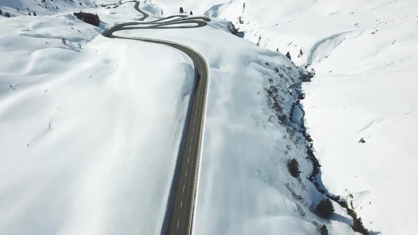 An aerial view of a paved road winding through a rural snowy landscape