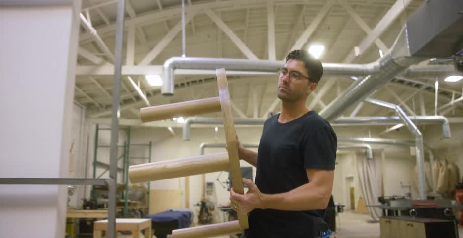 A man carries a table through a workshop