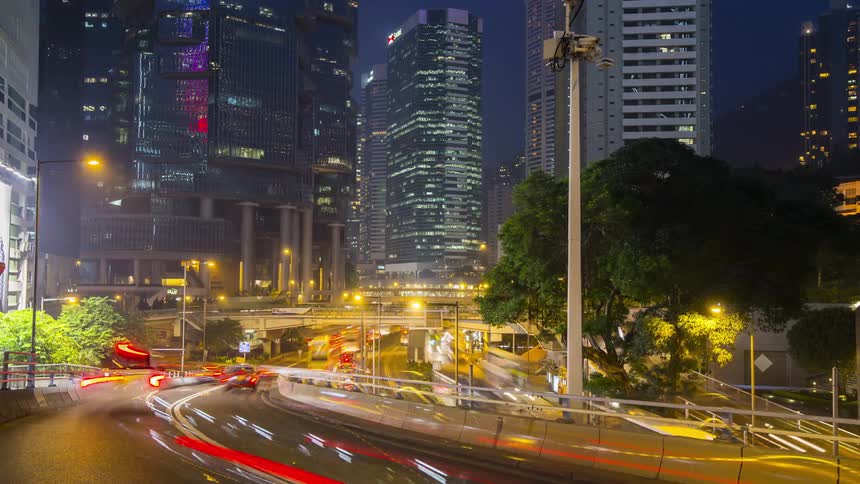 Time lapse of cars driving on a highway ramp in a city with high rise buildings at night time