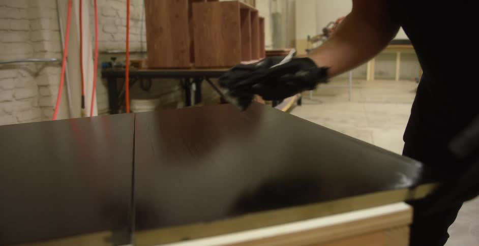A person in a workshop with gloves polishing wood with a wall in the background