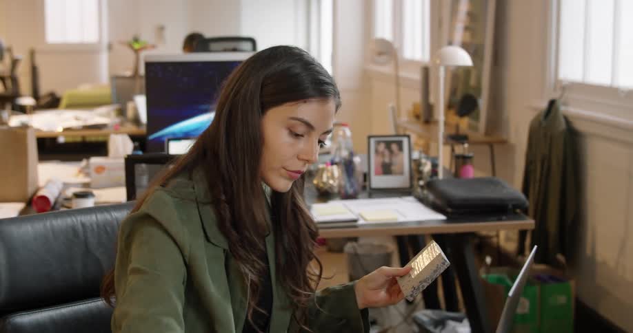 A woman sitting at a desk in a design office picks up a stone sample and enters information onto her laptop