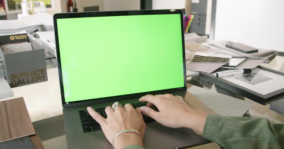 A man types at his desk cluttered with books and papers and picture frames