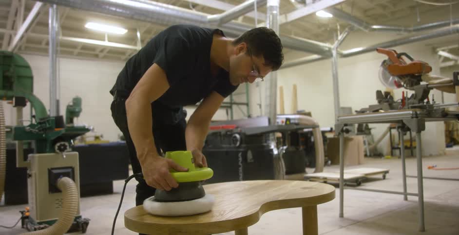 A man in a workshop polishes a table