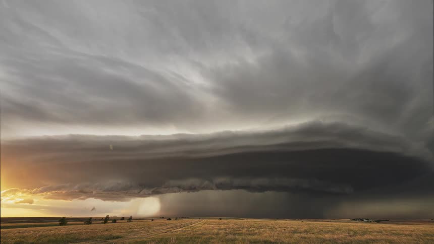Dark clouds floating above a rural field during a rainstorm at sunset