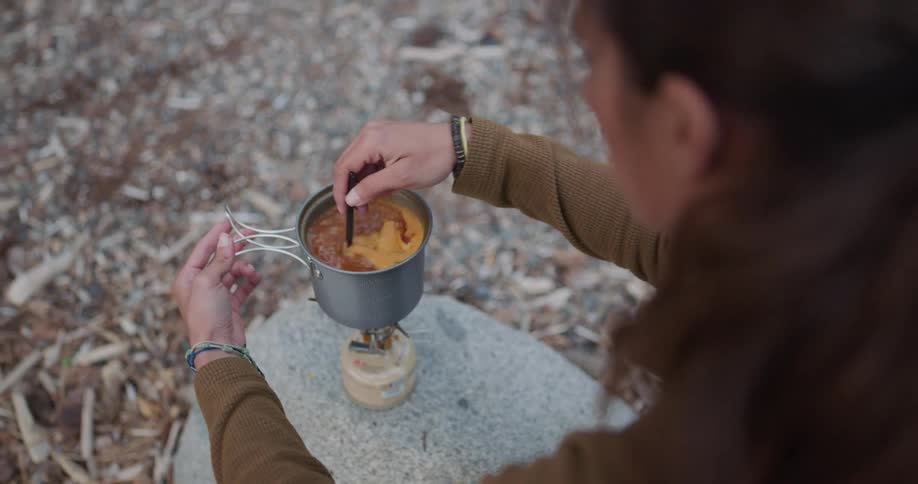 Woma cooking a meal in a small por over a portable stove while camping